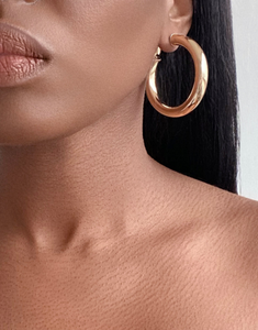 Close-up of a woman wearing elegant Cairo Large Clip-On Hoop Earrings in premium gold-plated brass, showcasing their substantial size and glossy finish. The earrings add a touch of sophistication to her poised appearance.