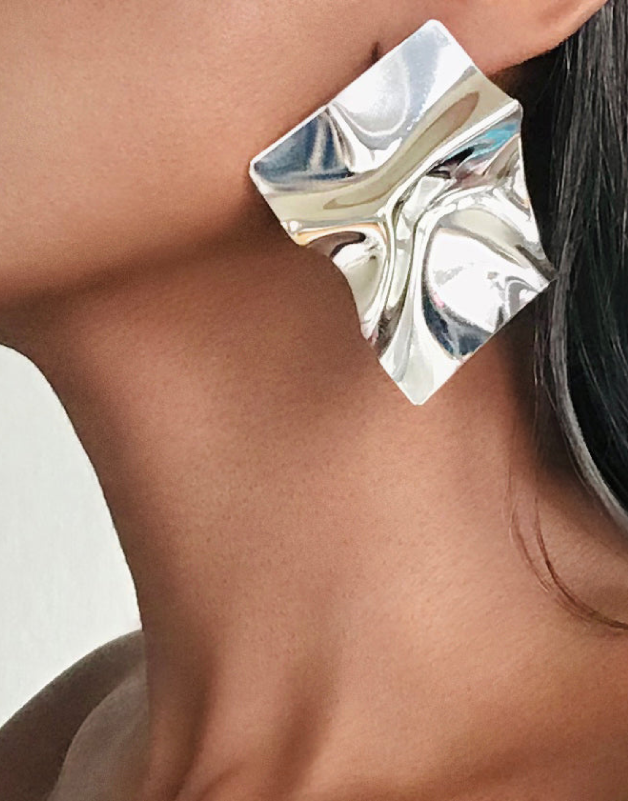 Close-up of a woman's profile wearing LUNIT Silver Square Stud Earrings, which feature a unique, sculptural and mirrored design in premium silver-plated brass. The earrings display a striking geometric shape that reflects light, adding a sophisticated and modern touch to her look.